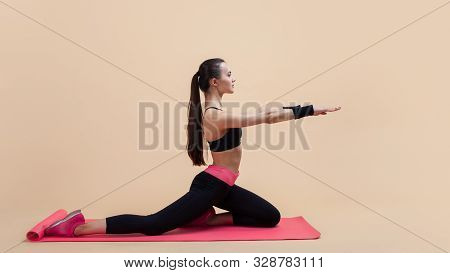 Young Attractive Girl With A Ponytail, Brunette, Sitting In The Pose Of A Pigeon With His Hands On A