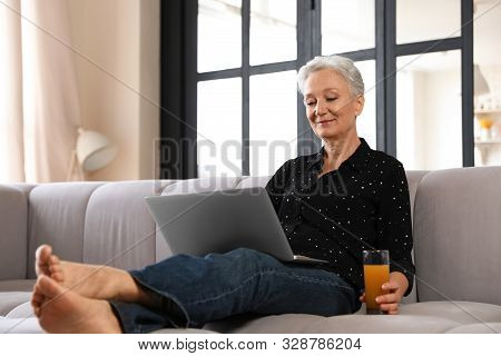 Mature Woman With Laptop And Drink Sitting On Sofa At Home. Smart Aging