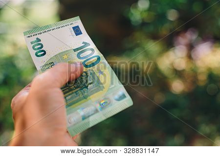 Male Hand Holding 100 Hundredth Euro Banknote On Green Background Outdoors, Closeup