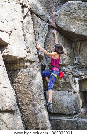 The Girl Climbs The Rock. Rock Climber Is Training On Natural Terrain. Extreme Hobby. A Woman Overco