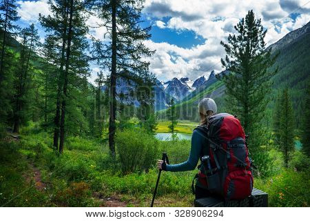 Girl Tourist With Backpack And Poles Looking At The Beautiful Summer Landscape With Mountain Peaks. 