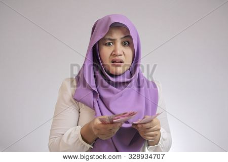 Portrait Of Indonesian Muslim Woman Looked Confused With Her Rupiah Money, Complaining Too Small Sal