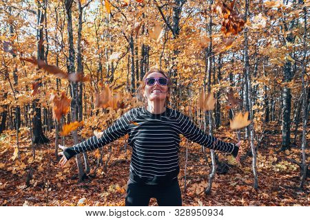Woman Throwing Autumn Leaves In The Air, In The Forest, Full Of Fall Colors. Concept For Autumn And 