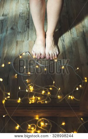 Woman Legs Near Christmas Garland On The Floor. Holiday Prepararions.