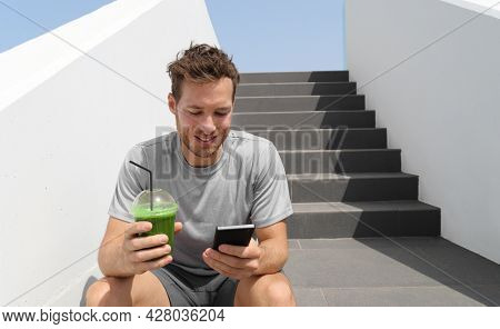 Green smoothie juice drink man drinking detox diet protein shake using mobile phone app for tracking nutrition diet meal plan. Healthy lifestyle.