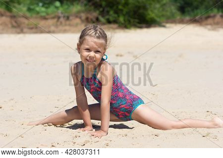 Caucasian Little Girl Of Five Years Old In Swimsuit On Sand Beach Making Leg-split In Summertime