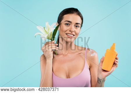 Cheerful Woman With Sunblock And White Lily Looking At Camera Isolated On Blue