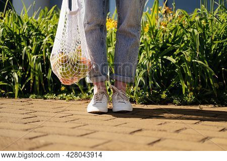 Woman In Jeans Standing And Holding White Mesh Bag With Fruits. Eco Friendly, Reusable Shopping Bag.