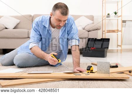 Middle-aged Man Installing Furniture Reading Self-assembly Manual At Home