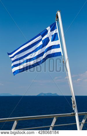 Greek Flag On The Blue Sky And Blue Sea Background At The Aft Of A Ferry Boat. Vertical
