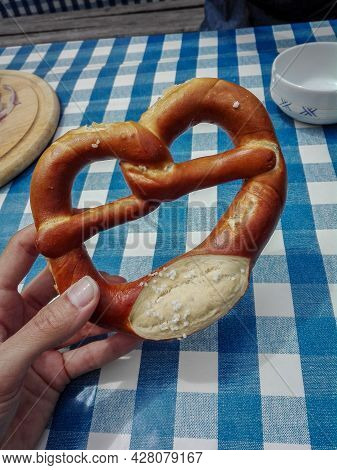 Pretzel Bread Hold By Left Hand On Top Of Blue Checkered Tablecloth