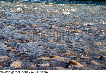 Sun Glare On Surface Water And Smooth Stones At Bottom Stream, Background. Transparent Water In Rive