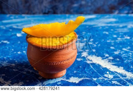Mango Pulp In Earthen Bowl With Ripe Mango Cut Isolated On Bluish Background