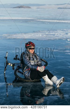 Woman Sitting Near Her Bike On Ice. The Girl Cyclist Stopped To Rest. She Sits On The Wheel And Enjo