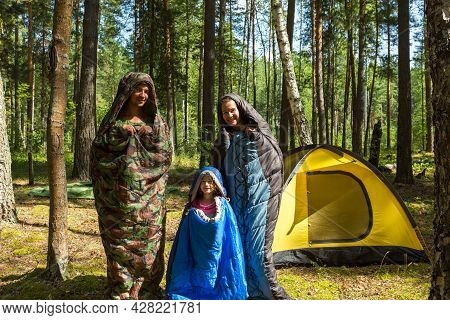 Family Of Tourists From A Father, Mother And Little Daughter Pose In Sleeping Bags Near A Tent. Fami
