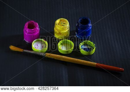 Stock Photo Of Pink , Blue, Yellow Watercolor Open Glass Bottle With Their Caps And One Wooden Paint