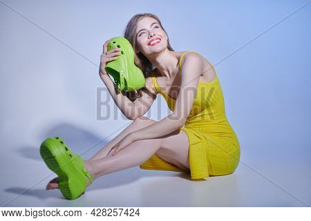 Full length portrait of a beautiful blonde girl  in bright clothing sitting on the floor in light green sabot. Fashion studio shot with copy space.