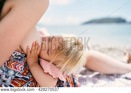 Mom Breastfeeds A Little Girl While Sitting On The Beach By The Sea
