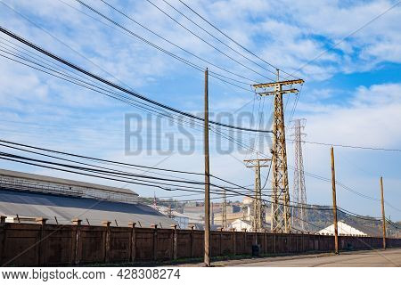 Tall Metal Power Towers And Wood Power Poles Carry Lines Through A Large Industrial Facility Under B