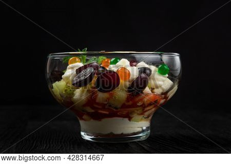 Salad from grapes apples pears kiwi oranges with mascarpone chease and cream. Healthy fresh fruit summer salad in glass bowl on black wooden background with copy space.