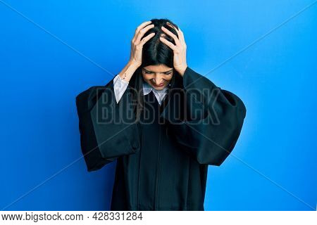 Young hispanic woman wearing judge uniform suffering from headache desperate and stressed because pain and migraine. hands on head. 
