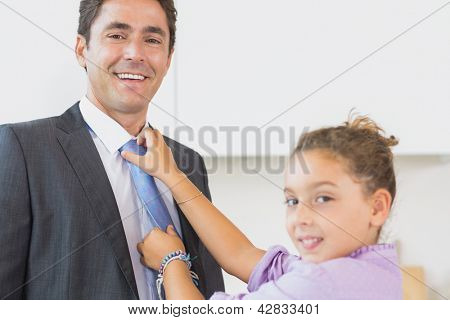 Filha sorridente fixação laço pai na cozinha antes do trabalho