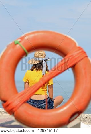 Young Skinny Girl With Straw Hat And Yellow T-shirt Inside An Orange Plastic Life Buoy