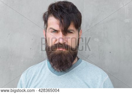 Bearded And Shaggy. Bearded Man With Stylish Haircut On Grey Wall. Unshaven Caucasian Guy Wearing Th