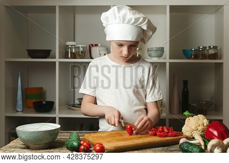 Cute Boy Chef Cutting Vegetables For Salad. Child Chef Cook At The Kitchen. Boy Wearing Chef Uniform