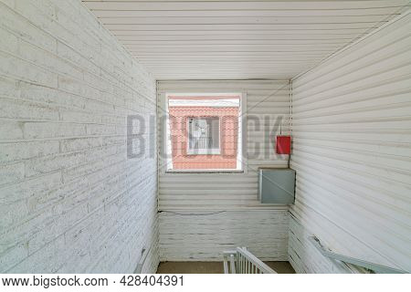 White Wall With Square Window With A View Of A Window And Hallway From The Building Across