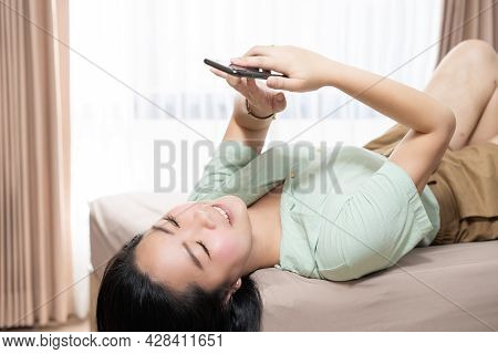 Beautiful Asian Woman Is Lying Down And Playing Mobile On The Bed In Her Bedroom With A Pastel Green