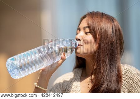 Asian Woman Drinks Big Bottle Water In Outdoor Green Bokeh Tree Background.
