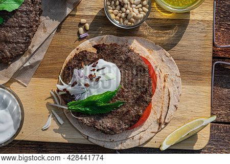 Lamb Kebab Patties Served With Mint Dip, Crunchy Salad, Pitta Bread And Raw Red Onions.