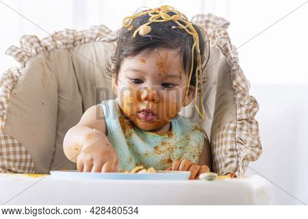 Adorable Little Funny Girl Of 12 Months Eating Spaghetti With Hand While Sitting In High-powered Cha