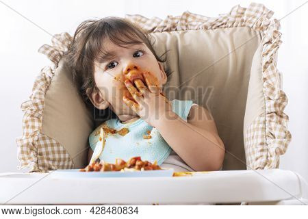 Adorable Little Child Funny Girl Eating Spaghetti With Spoon While Sitting In High-powered Chair At 