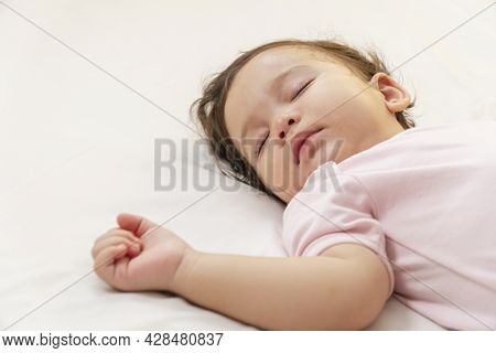 Little Baby Girl 12 Months Wearing Pink Cloth Sleeping On White Bed At Home. Adorable One Year Old T