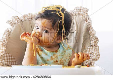 Adorable Little Child Funny Girl Eating Spaghetti With Spoon While Sitting In High-powered Chair At 
