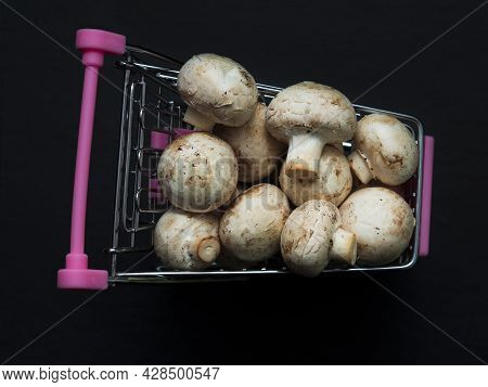 A Lot Of White Champignons Are Lying In A Small Shopping Trolley. Noble Mushrooms In A Toy Metal Car