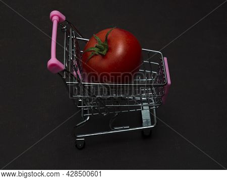 One Red Tomato Is Lying In A Small Shopping Trolley. A Farmer's Vegetable In A Toy Metal Cart.