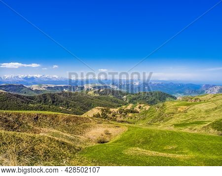Green Grass On The Yellow Spring Alpine Meadows Of The Gumbashi Pass. Snow Covered Huge Mountain Elb