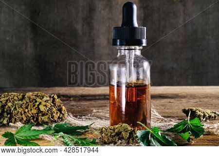 Medical Cannabis Resin Extract Concentrate In Bottle Of Medicine Dropper. Next To Marijuana Buds And