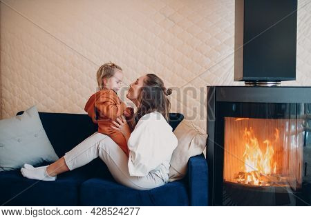 Mother And Child Sitting And Playing On Sofa Near Fireplace. Single Parenting. Mom And Baby Child. P