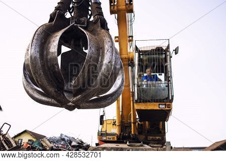 Man Operating Excavator Industrial Machine With Claw Attachment Used For Lifting Scrap Metal In Junk
