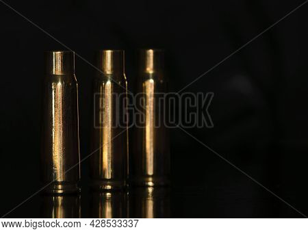 Spent Cartridges On A Black Background. Three Empty Cartridge Cases Are Lined Up Side By Side. Close