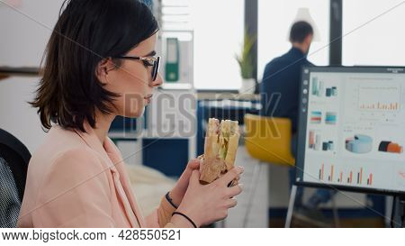 Entrepreneur Woman Eating Tasty Sandwich During Takeout Lunchbreak Working At Financial Graphs In St