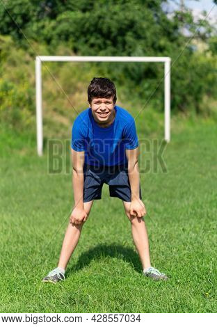 teenage boy exercising outdoors, sports ground in the yard, standing as a goalkeeper at the soccer gate, healthy lifestyle