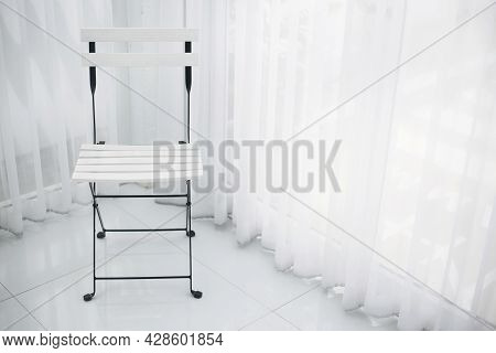 White Chair With Black Steel Frame On Tile Floor In The Coner Of Room With White Curtain