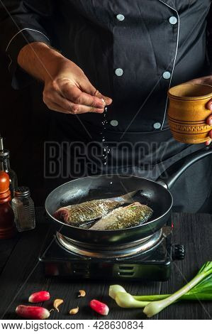 Cook Or Chef Prepares Fresh Fish In Pan Sprinkling Salt With Ingredients. Preparing To Cook Fish Foo