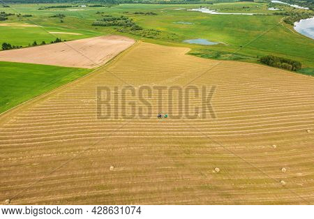 Aerial View Tractor Collects Dry Grass In Straw Bales In Wheat Field. Special Agricultural Equipment