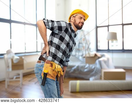 repair, construction and building concept - male worker or builder in helmet having back ache over home room background